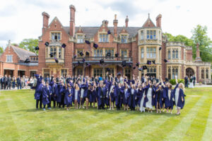 Graduates in purple gowns throwing caps in the air outside a historic brick campus building.