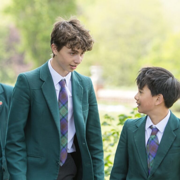 Group of students in green blazers walking and chatting in a sunny outdoor setting. (School uniforms, trees in the background)