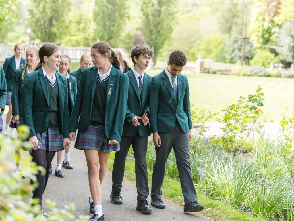 Group of students in green blazers walking along a park path outdoors.