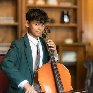 Young boy in a green blazer playing a cello indoors, focused on the bow.”