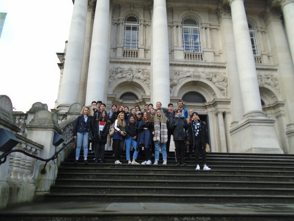 Group of students posing on stone stairs in front of a grand historic building with tall columns and arches