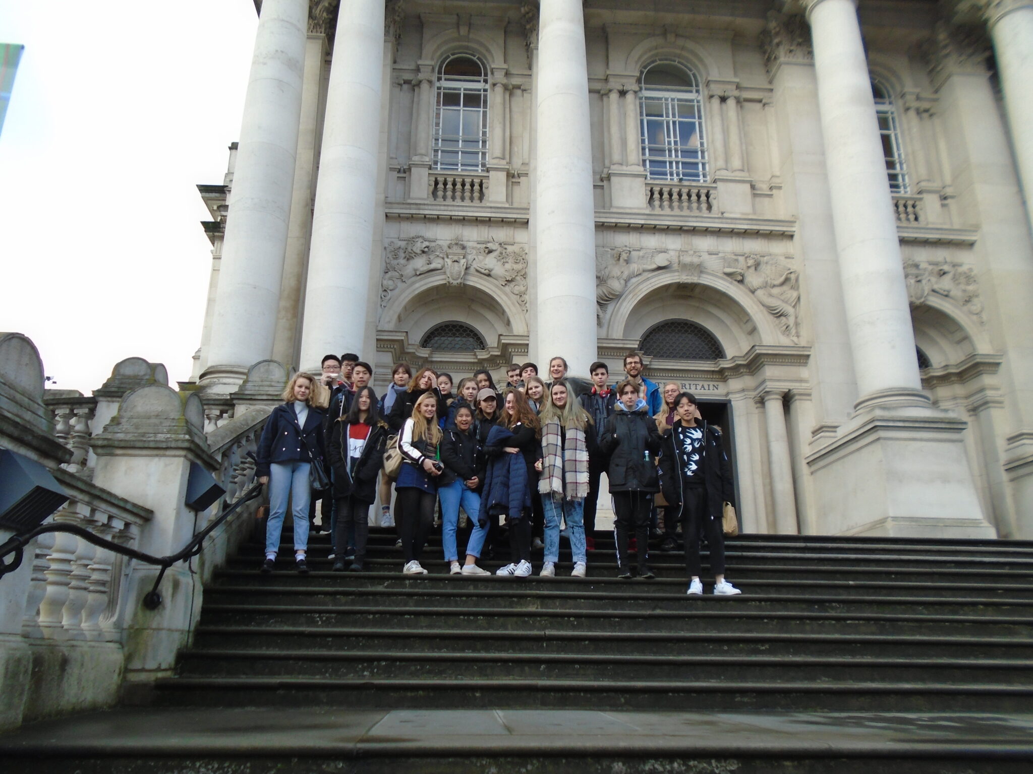 Group of students posing on stone stairs in front of a grand historic building with tall columns and arches