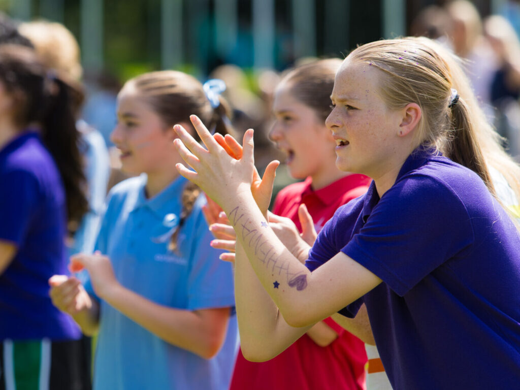 Group of young people cheering and clapping at an outdoor event in colorful shirts.