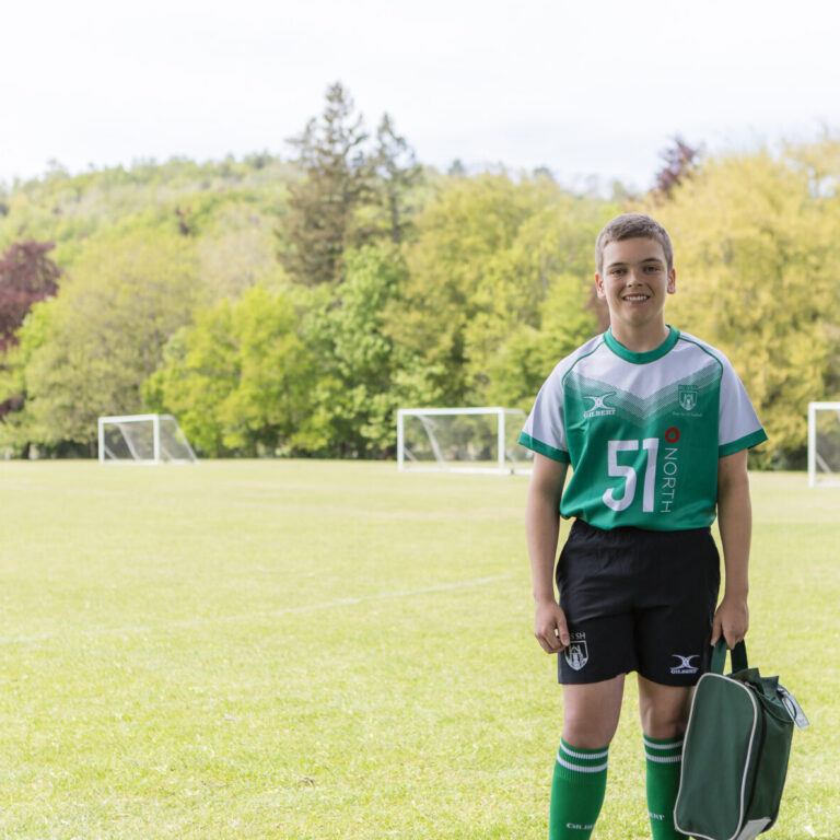 Young soccer player in a green jersey with number 51 standing on a sunny field, holding a green sports bag.